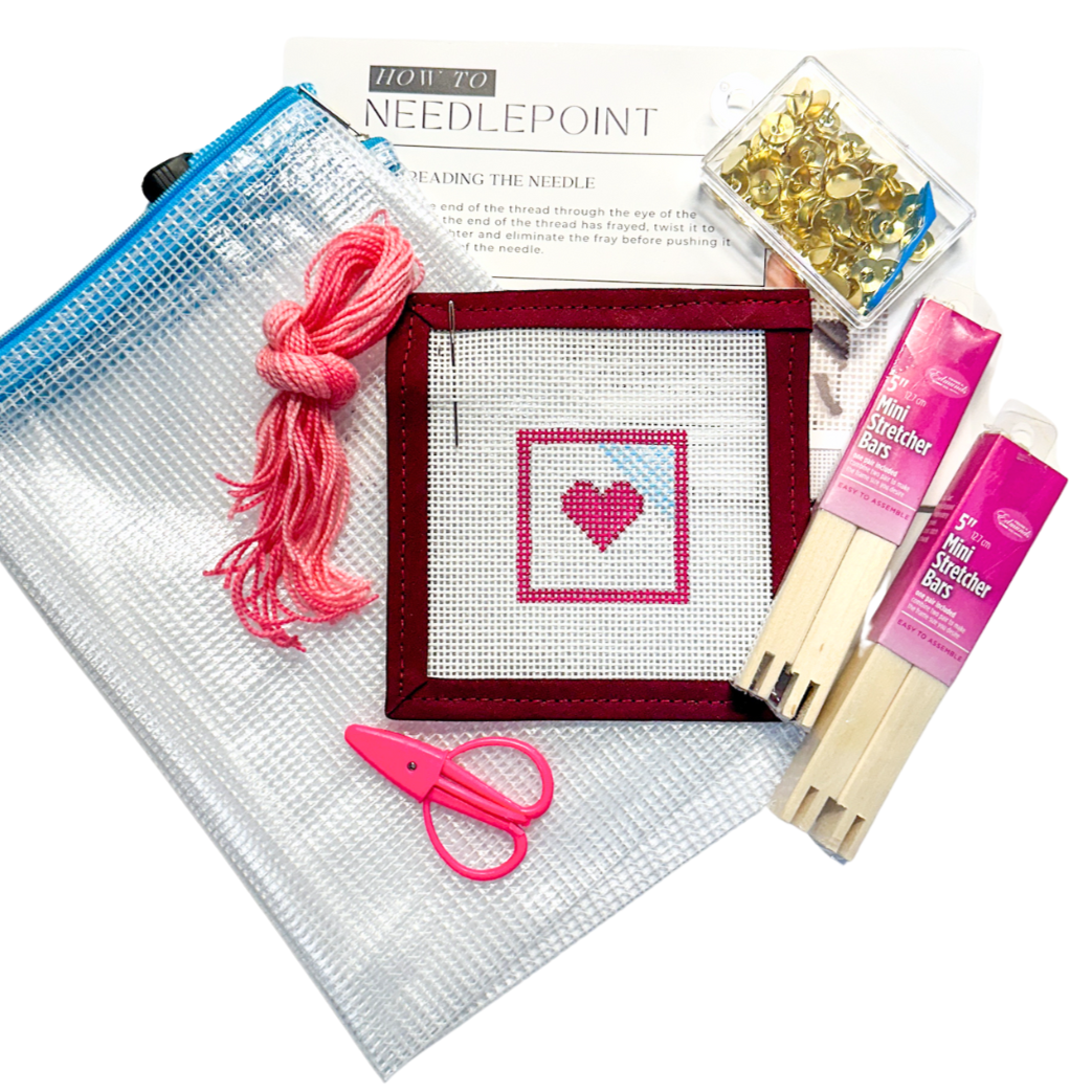 Beginner needlepoint kit for online Needlepoint Basics Class, featuring a heart canvas, stretcher bars, pink thread, scissors, tacks, mesh project bag, and instructional guide from Spellbound Stitchery.