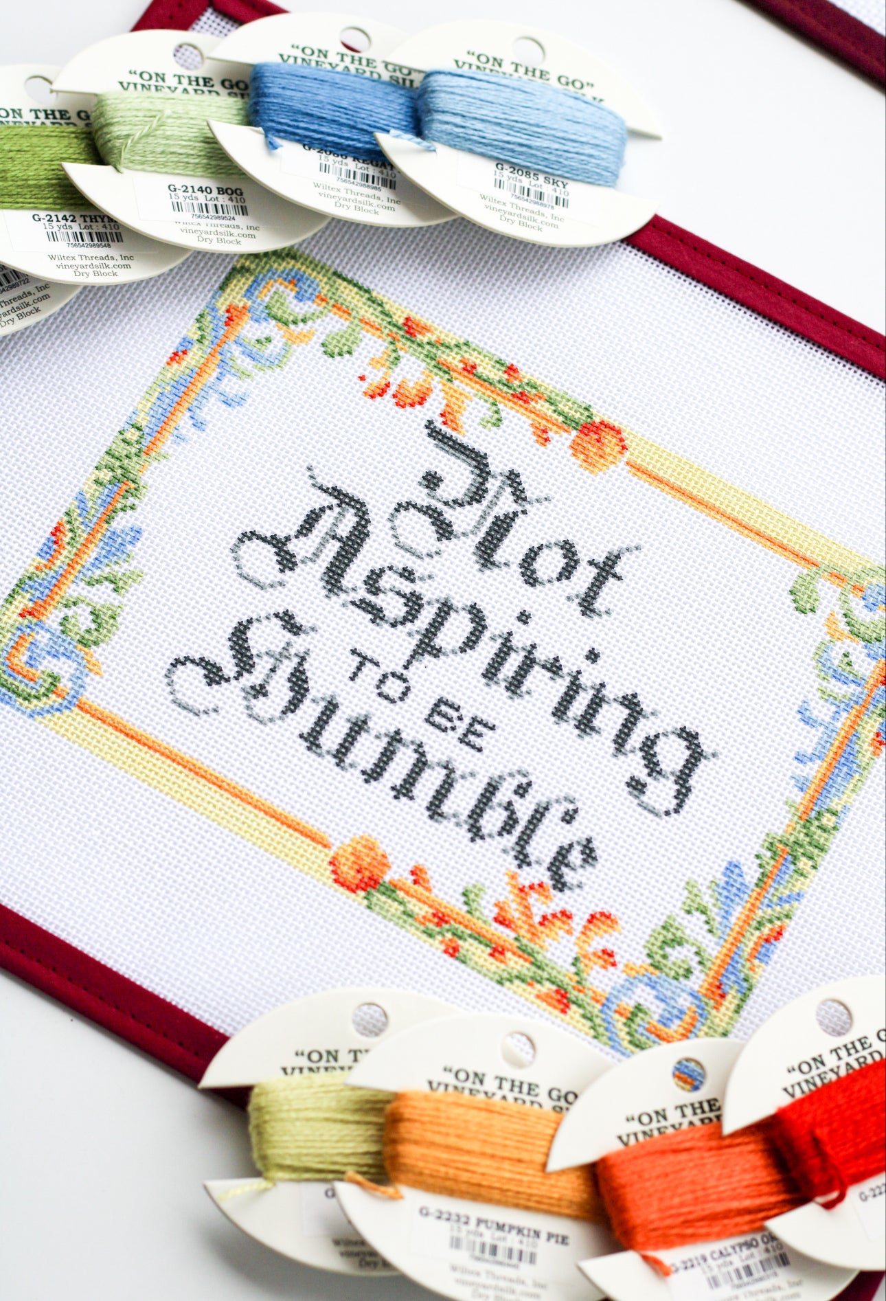 Not Aspiring to Be Humble needlepoint canvas shown with coordinating Vineyard Silk thread spools in vibrant colors for stitching inspiration.