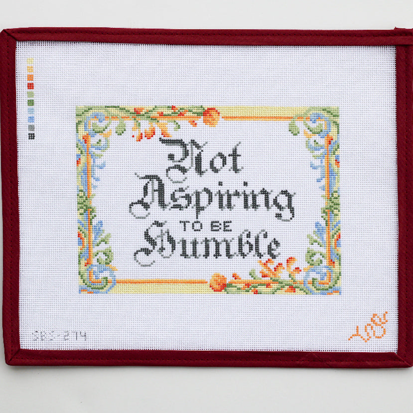Close-up of the Not Aspiring to Be Humble needlepoint canvas, featuring detailed border work and calligraphy in a classic stitch-painted layout.