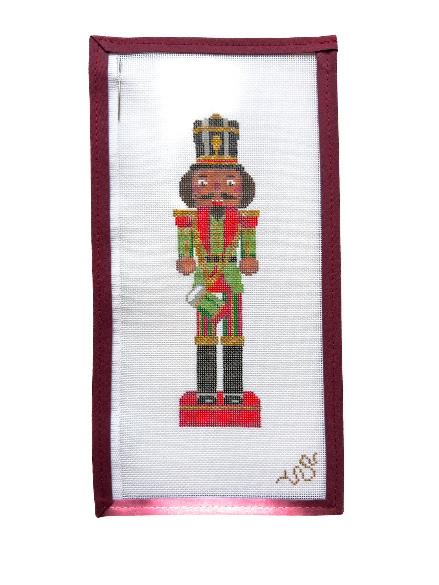 Hand-painted needlepoint canvas of a traditional Christmas nutcracker soldier with rich brown skin, festive red and green uniform, and gold crown, part of the Heritage Christmas Collection by Spellbound Stitchery.
