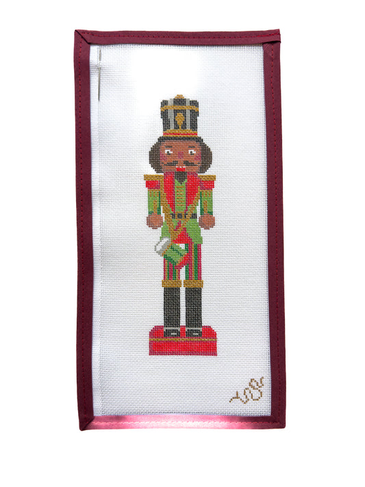 Hand-painted needlepoint canvas of a traditional Christmas nutcracker soldier with rich brown skin, festive red and green uniform, and gold crown, part of the Heritage Christmas Collection by Spellbound Stitchery.