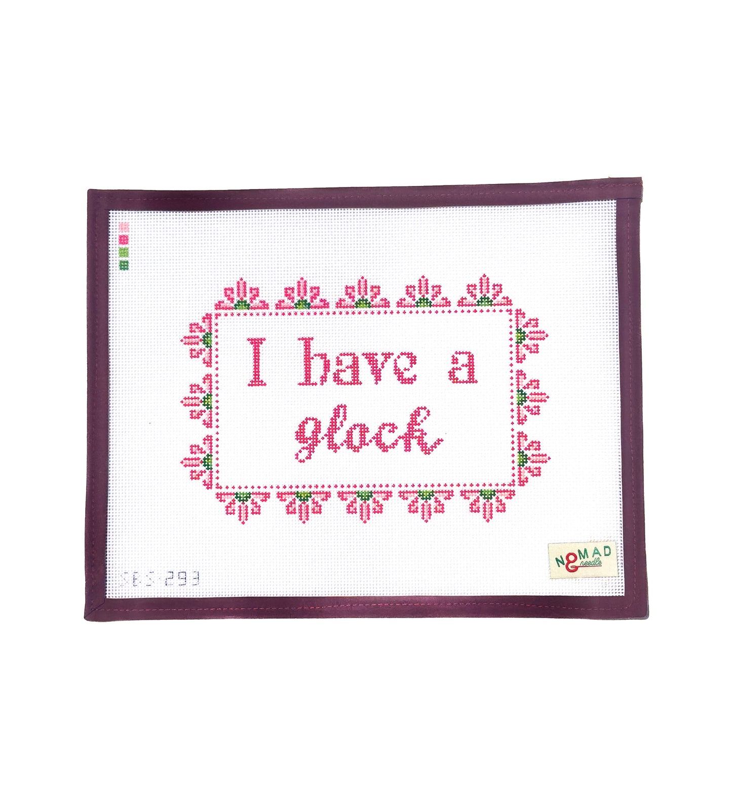 Hand-painted needlepoint canvas with the phrase “I have a glock” in pink cross-stitch lettering, framed by a floral border, designed by Nomad & Needle.
