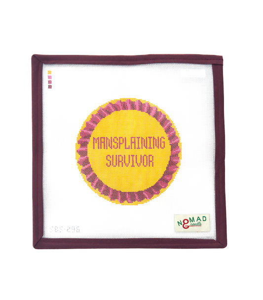 Hand-painted needlepoint canvas featuring a bold yellow and pink ribbon that reads “Mansplaining Survivor,” designed by Nomad & Needle for feminist stitching.