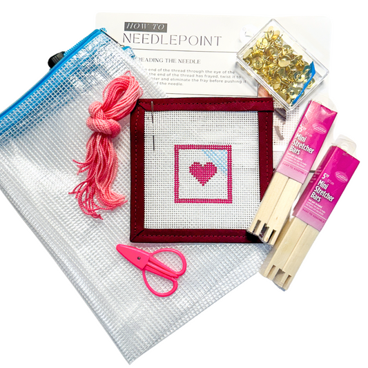 Beginner needlepoint kit for online Needlepoint Basics Class, featuring a heart canvas, stretcher bars, pink thread, scissors, tacks, mesh project bag, and instructional guide from Spellbound Stitchery.